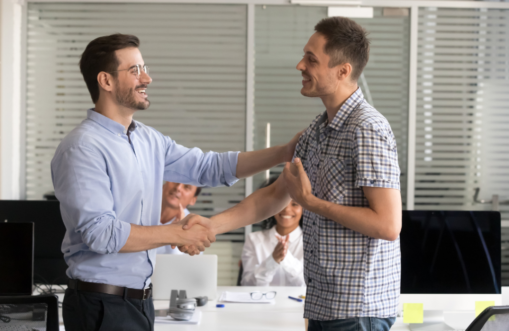 Recovered employee returning to work, greeted by a manager with a handshake.